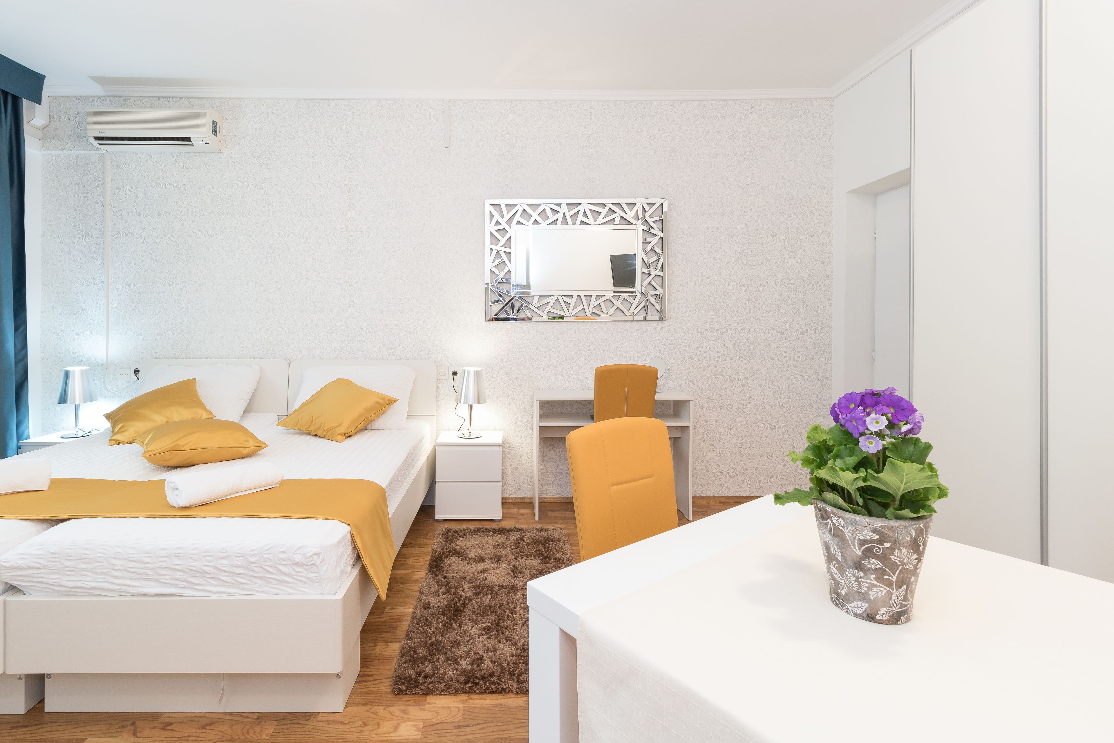 Una habitación de hotel moderna con una cama bien hecha, un escritorio y una silla. Hay una planta en maceta sobre el escritorio y un espejo en la pared.