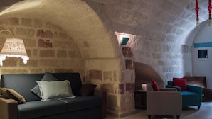 Una habitación acogedora con pared de piedra, un sofá oscuro, un sillón de tonos claros y una alfombra estampada.