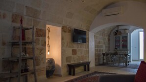 Una sala de estar acogedora con paredes de piedra, un televisor, una escalera de madera y un banco.