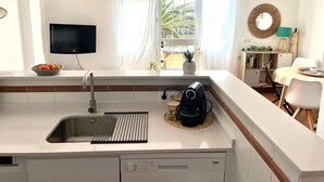 A modern kitchen with a built-in dishwasher, a sink with a strainer, a coffee maker, and a bowl of oranges on the counter.