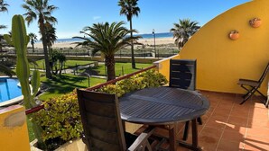 A patio with a round table and chairs, overlooking a beach and palm trees.