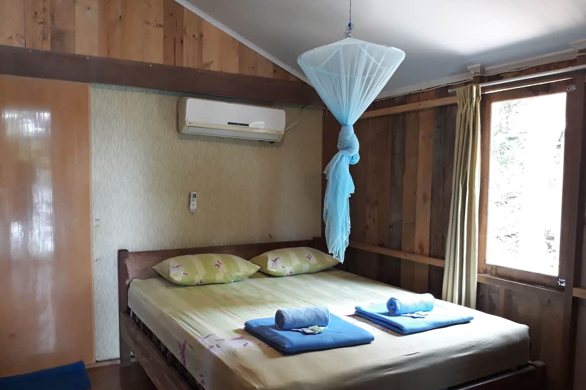 A wooden room with a bed, a mosquito net, an air conditioner, and a window with curtains.