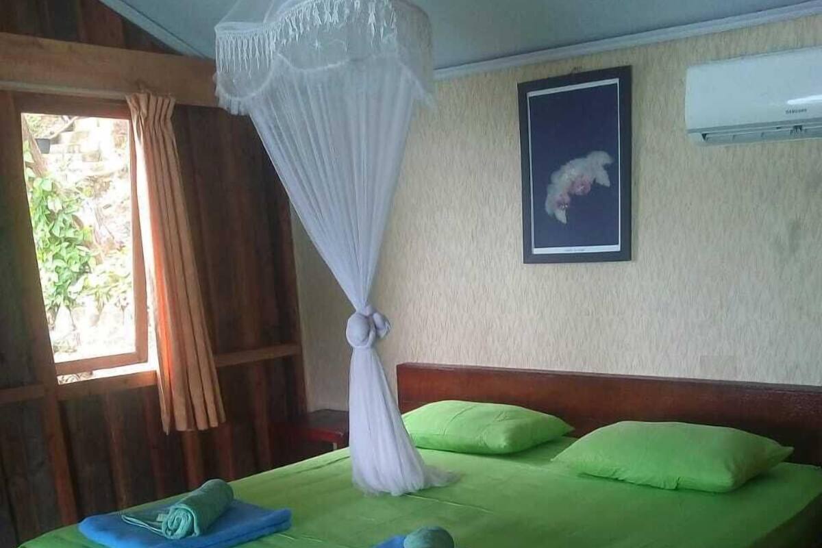 A bed with green bedding, a canopy, and two rolled towels.