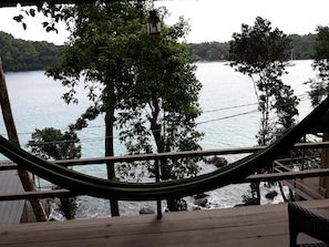 Een hangmat op een houten terras met uitzicht op een wateroppervlak, bomen en een boot in de verte.