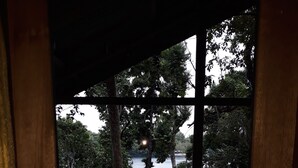 Vista a través de una ventana con marco de madera, mostrando un cuerpo de agua, árboles y un edificio con techo azul.