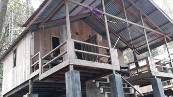 Une structure en bois surmontée d’un toit métallique, avec des piliers en béton et un escalier menant à un niveau supérieur.