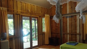 Una habitación de madera con dos camas, una hamaca y vistas al verdor exterior.