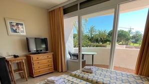 Habitación de hotel con dos camas, televisión, escritorio y vistas al exterior.