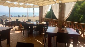 Un espacio al aire libre con mesas y sillas, con vista a la playa.