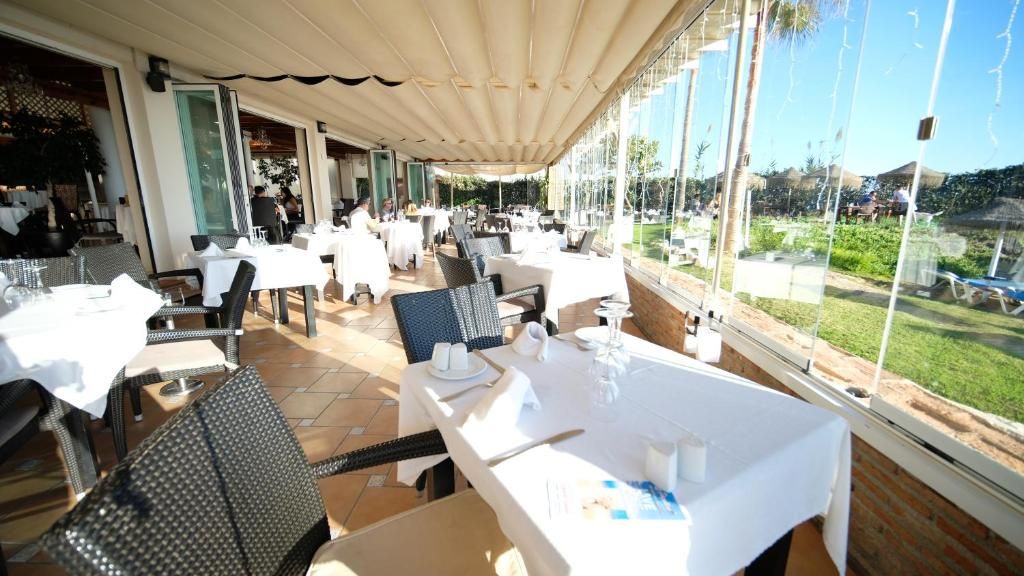 An outdoor dining area with tables and chairs, large windows, and a view of the landscape.