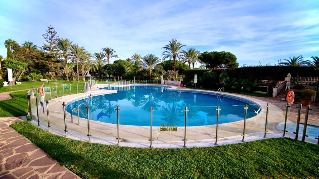 Una piscina rodeada por una terraza empedrada, con palmeras y follaje en el fondo.