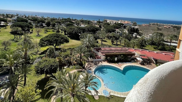 Un resort con piscina, palmeras y vistas al océano.