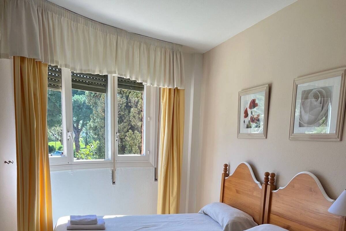 A hotel room with two beds, a wooden nightstand, and a window with curtains.