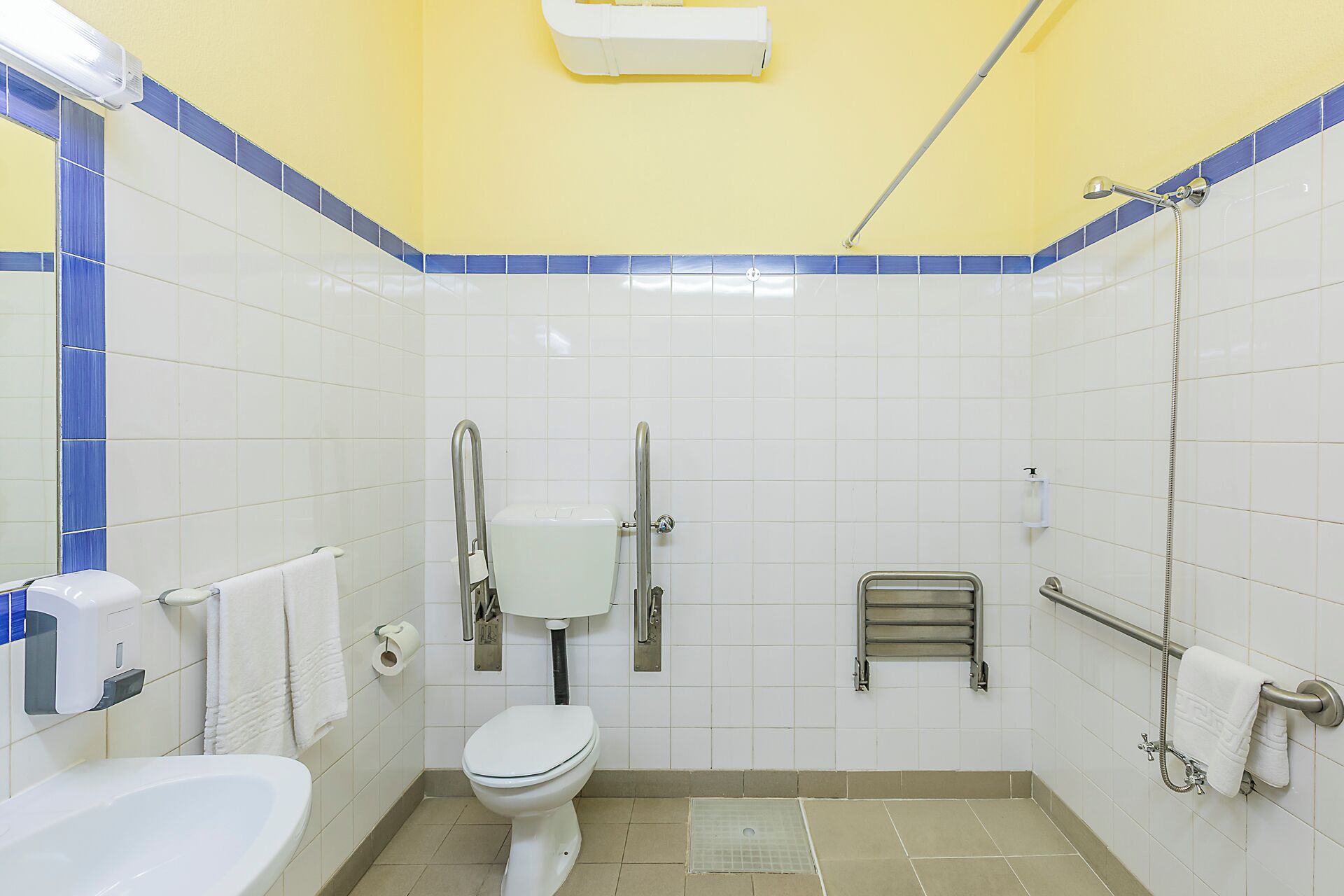 A bathroom with a toilet, hand dryer, and a shower.