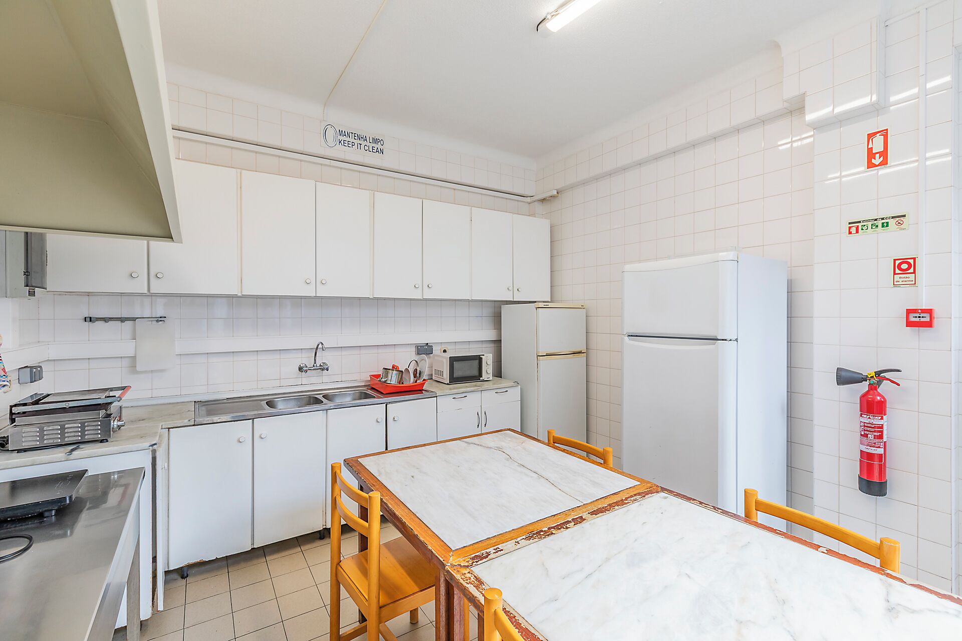 Una cocina con armarios blancos, un lavamanos, un microondas, un refrigerador y una mesa con sillas.
