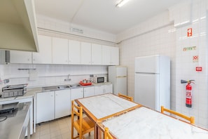 Una cocina con armarios blancos, un lavamanos, un microondas, un refrigerador y una mesa con sillas.