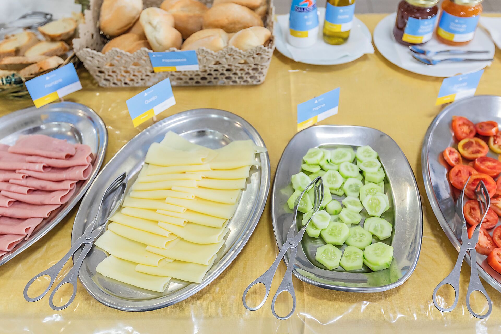 A buffet table with various food items including sliced ham, cheese, cucumbers, and tomatoes.