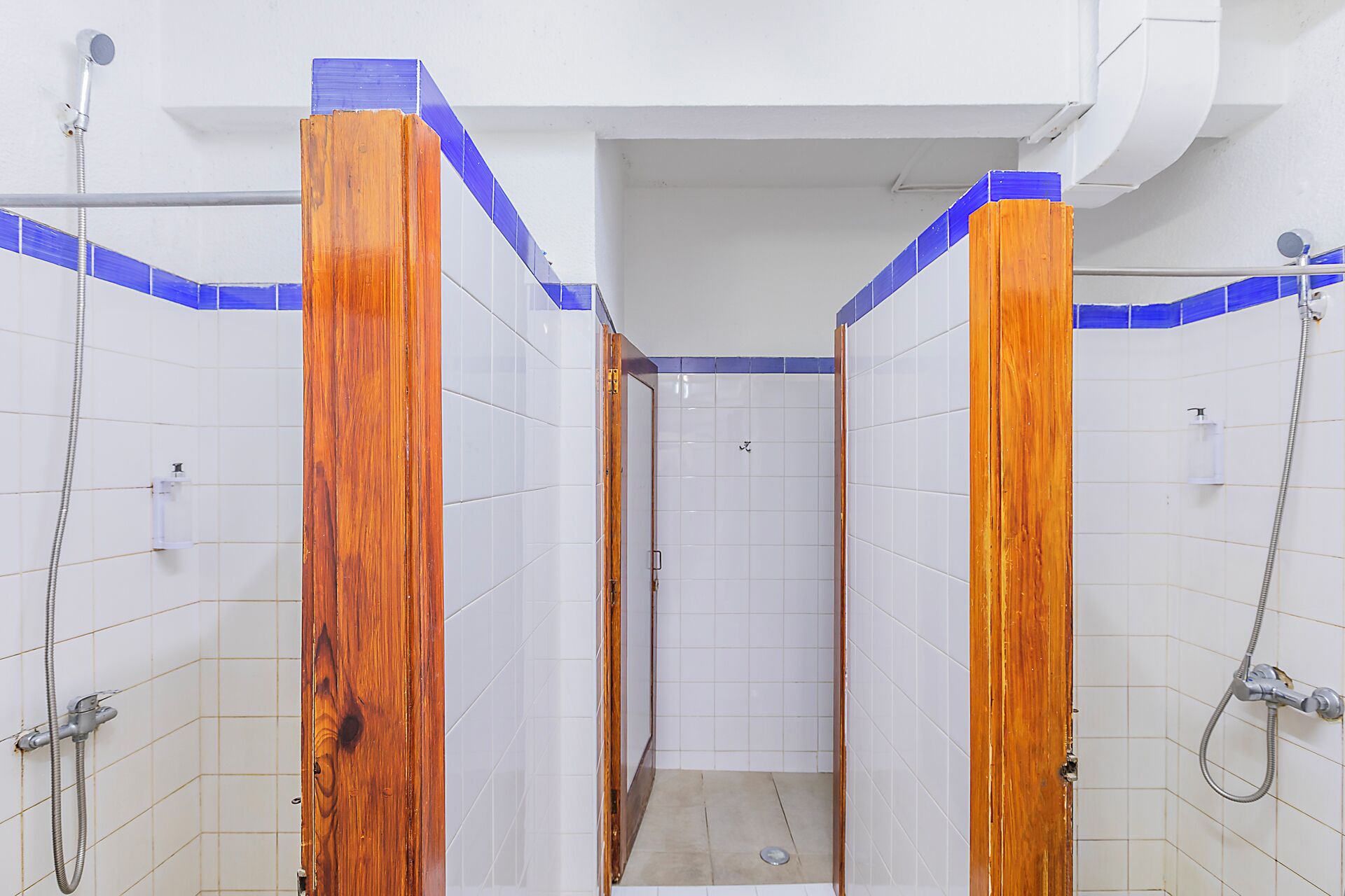 Un petit espace de douche, avec des murs carrelés de blanc et des touches de bleu, des encadrements de porte en bois et une pomme de douche bien visible.