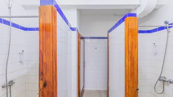 A narrow shower stall with white tiled walls and blue accents, wooden door frames, and a visible showerhead.