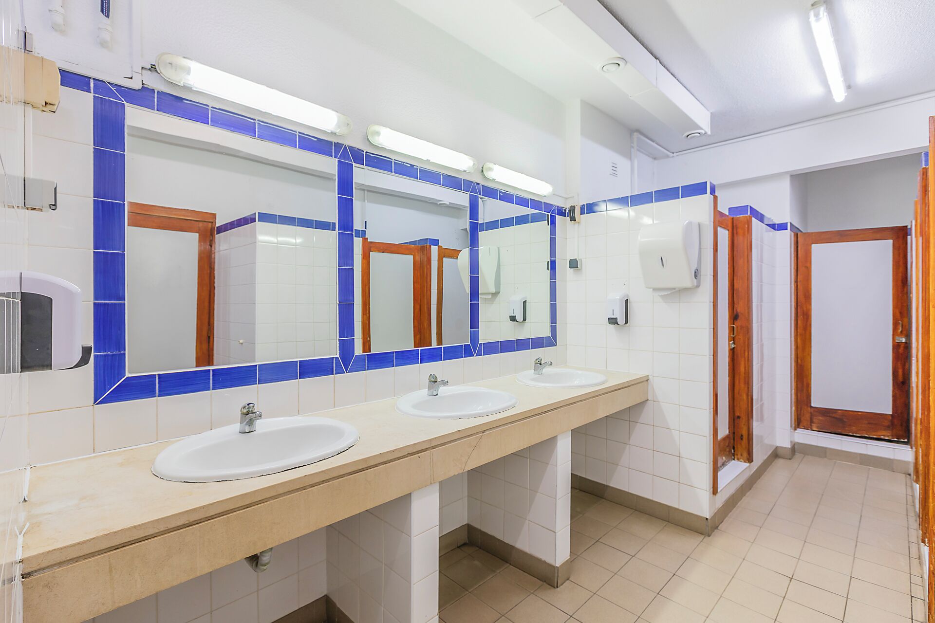 Un baño con tres lavamanos, un espejo grande y paredes con azulejos azules.