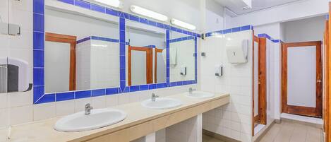 Un baño con tres lavamanos, un espejo grande y paredes con azulejos azules.