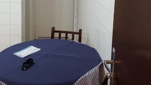 A room with a round table covered by a blue tablecloth, a chair, a door, and a light fixture above the door. - Kitnet em São Vicente (Sao Vicente)