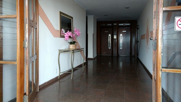 A hallway with a wooden door on the left, a mirror, and a potted plant on a console table. - Kitnet em São Vicente (Sao Vicente)