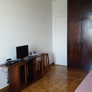 A room with a wooden desk, a computer, a television, and a small stool. - Kitnet em São Vicente (Sao Vicente)