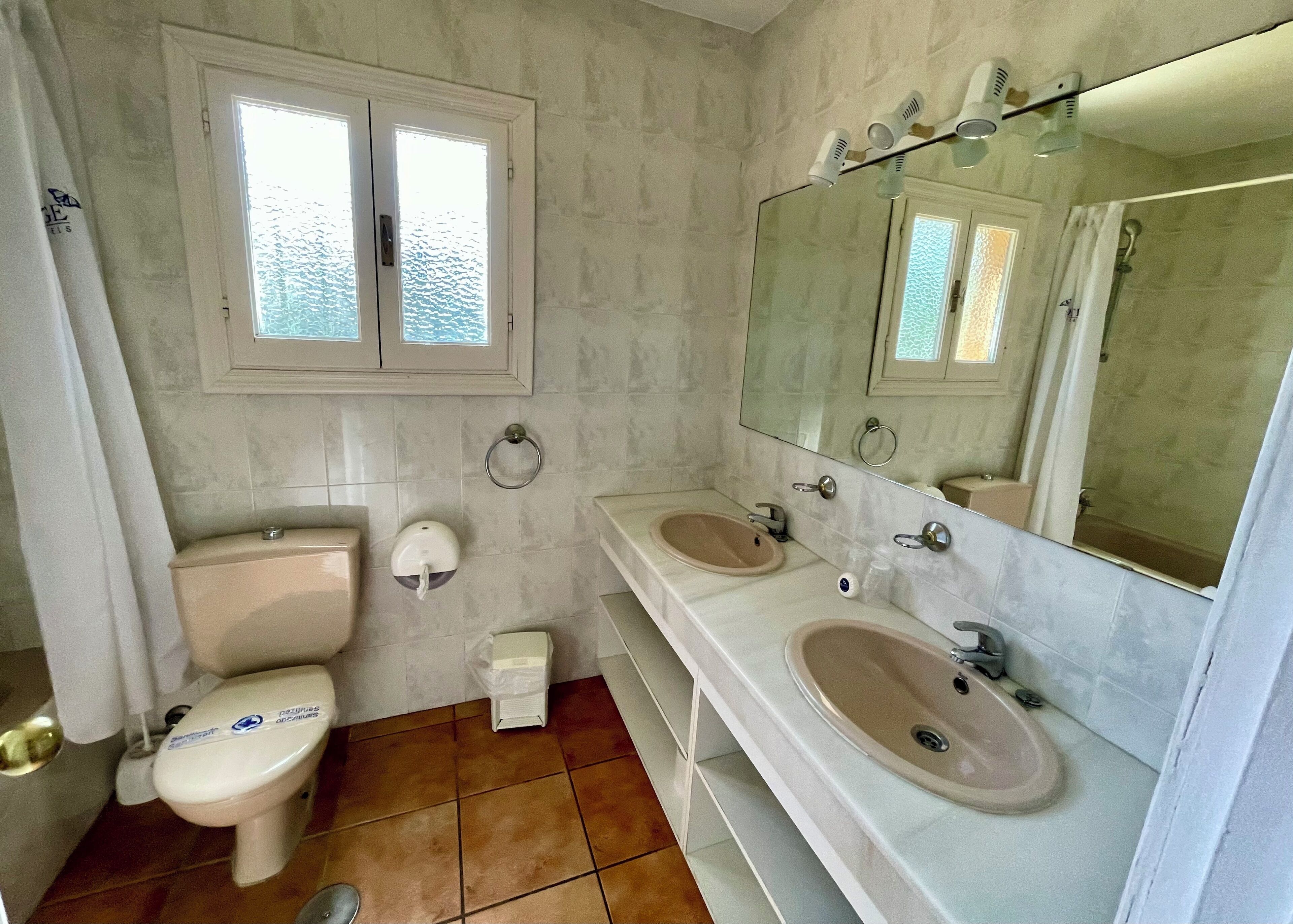A bathroom with a toilet, two sinks, a mirror, and a window.