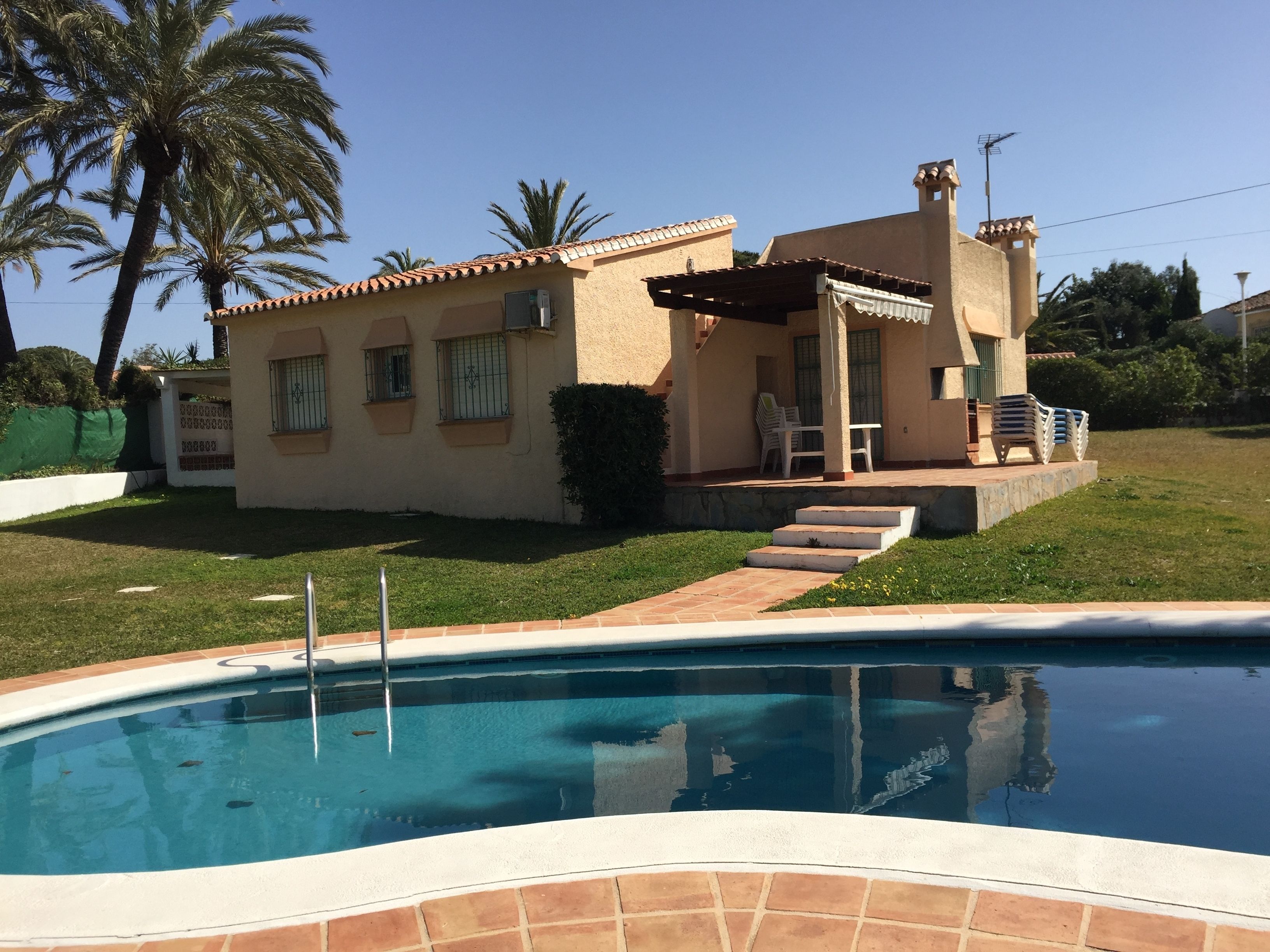 A house with a swimming pool, a patio with outdoor furniture, and a small garden area.