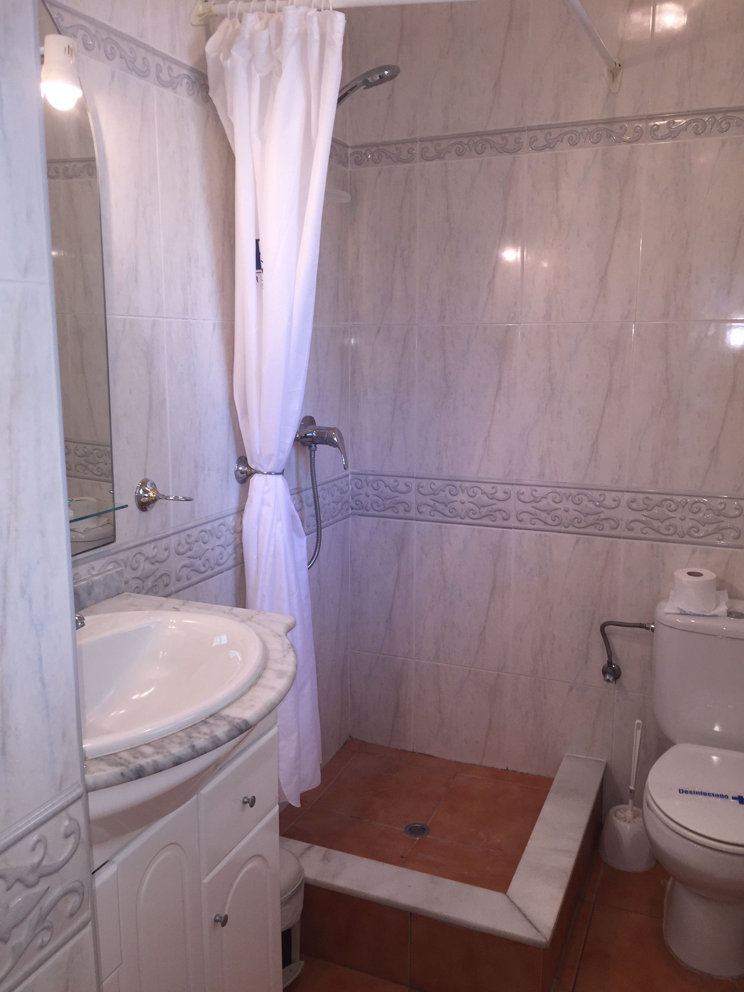 Ein Badezimmer mit Marmorwaschbecken, einer Dusche mit weißem Vorhang, einer Toilette und einem Bidet.