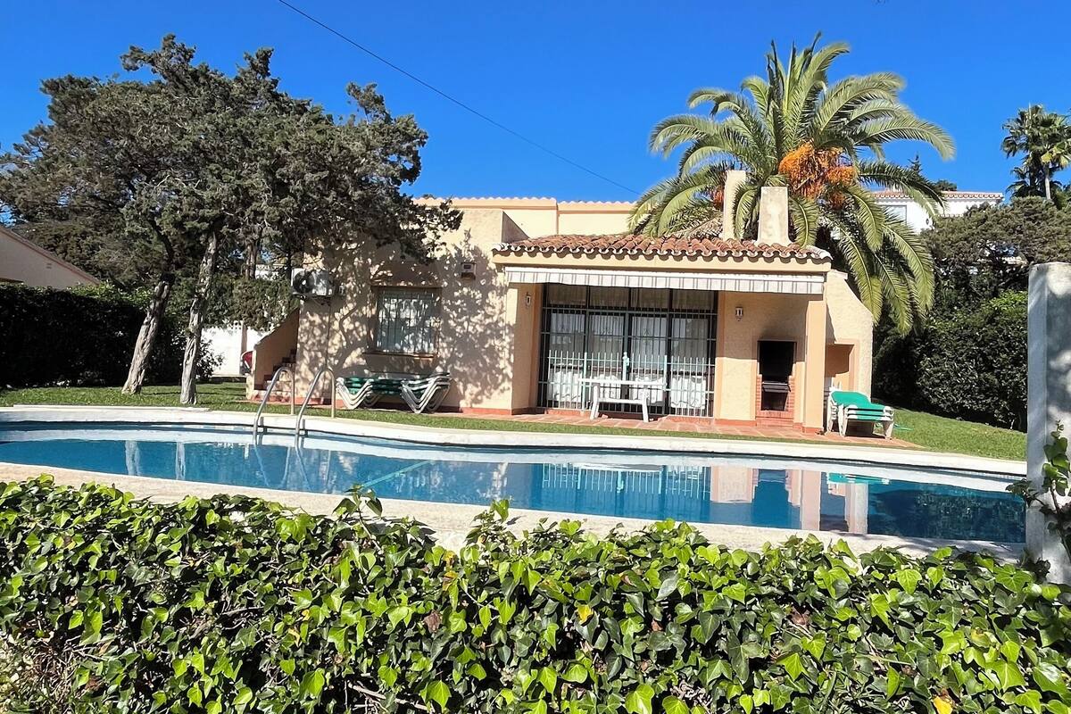 A house with a swimming pool, surrounded by greenery and palm trees.
