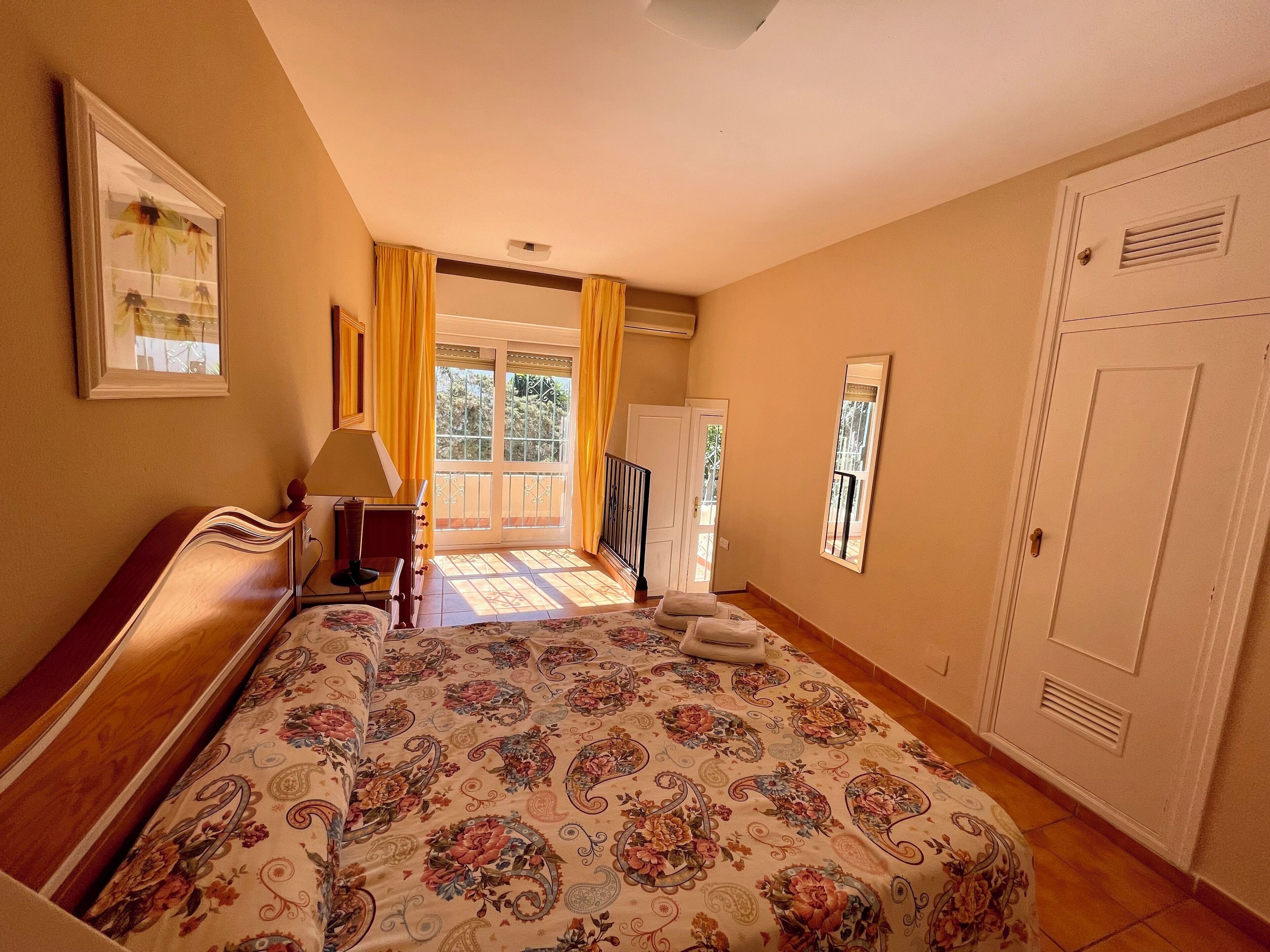 A bedroom with a bed, a nightstand, a window with curtains, and a door.