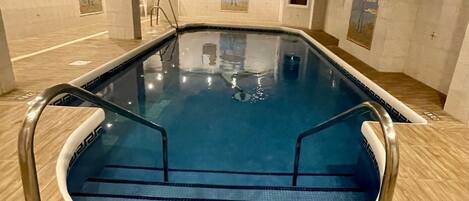 En inomhuspool med kristallklart blått vatten, omgiven av trägolv och väggar som pryds av konstverk.