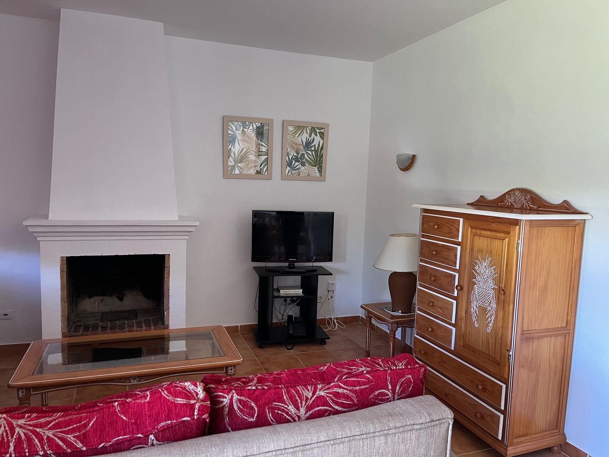 A living room with a fireplace, a television, a wooden cabinet, and a red patterned sofa.