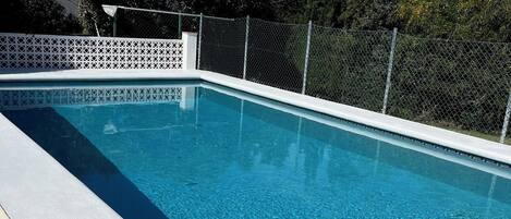 A rectangular swimming pool with clear blue water, surrounded by a white fence and a white lattice fence.