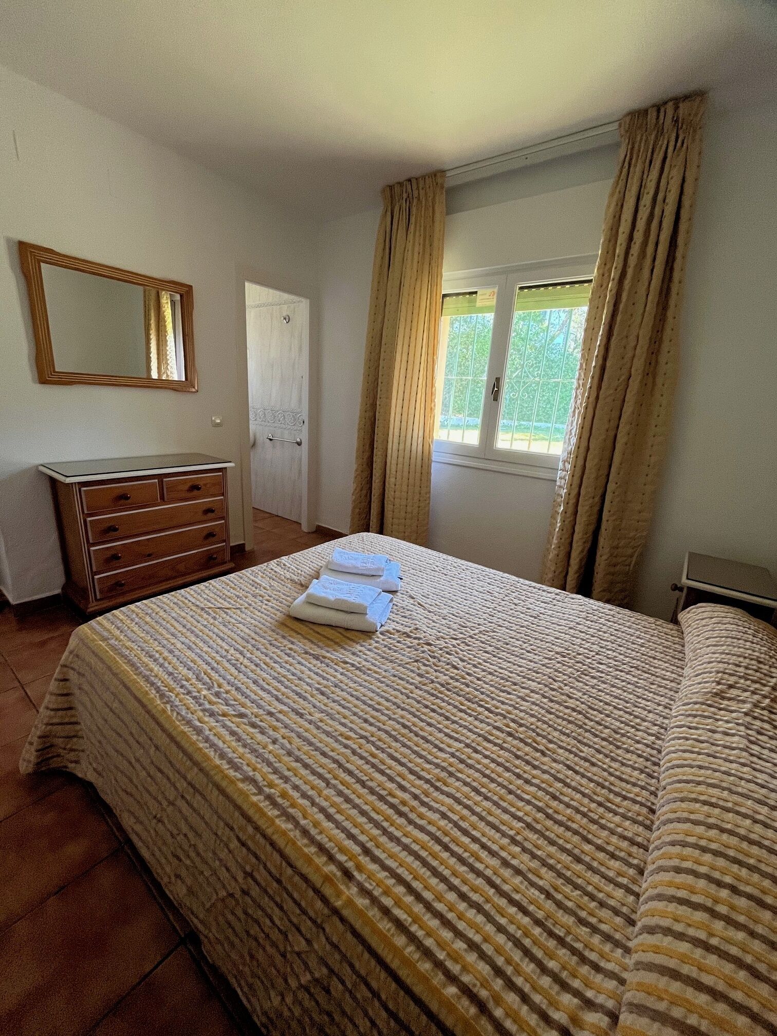 A bedroom with a bed, a dresser, a mirror, and a window with curtains.