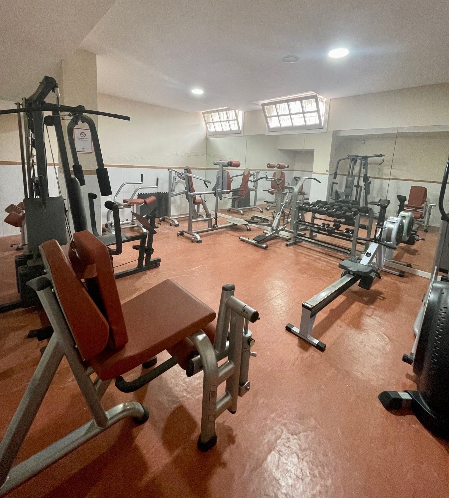 Ein Fitnessraum mit verschiedenen Trainingsgeräten, darunter Bänke und Gewichte, in einem offenen Bereich.