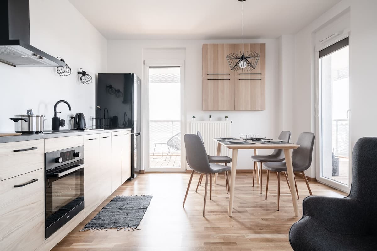 A modern kitchen with a built-in oven, a dining area with a table and chairs, and a large window providing natural light.