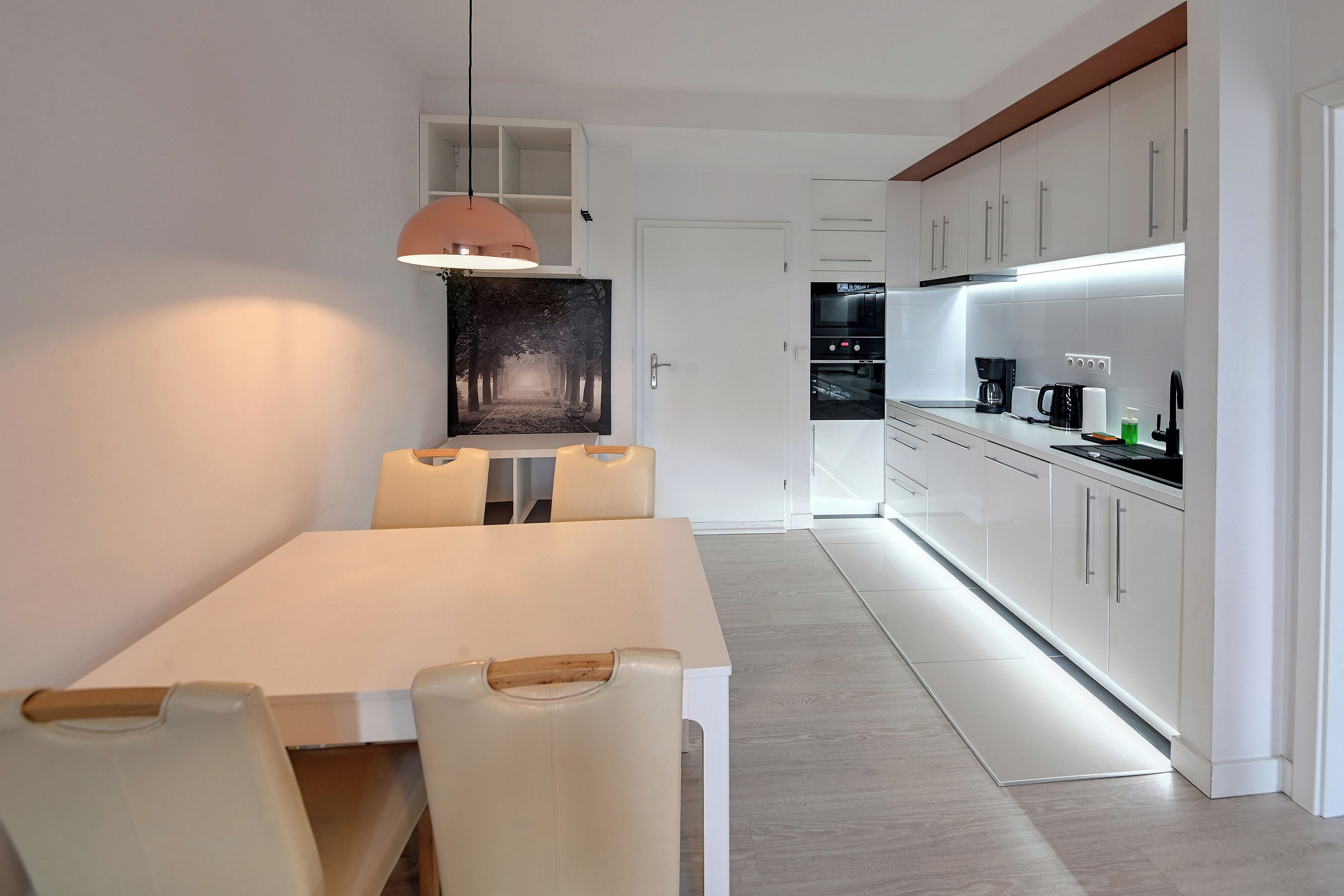 A modern kitchen with white cabinetry, a dining area with a white table and chairs, and a pendant light above the table.
