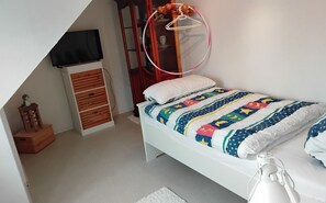 A bedroom with a bed, a television on a stand, a wardrobe, and a small wooden stool with a figurine.