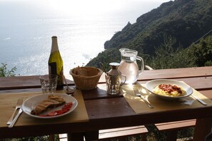 A wooden table with a plate of food, a bottle, a pitcher, and a glass. - Agririfugio Molini (Camogli)