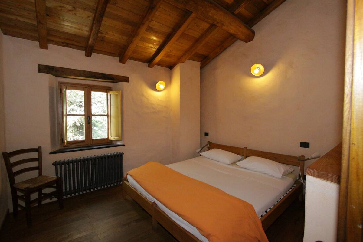 A bedroom with a wooden bed, a chair, a window, and two wall-mounted lights.