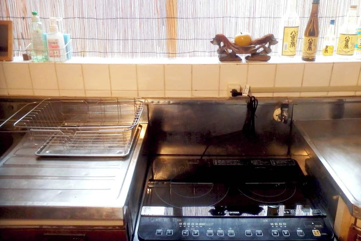 A kitchen with a stove, a sink, and a window with bottles on the sill.