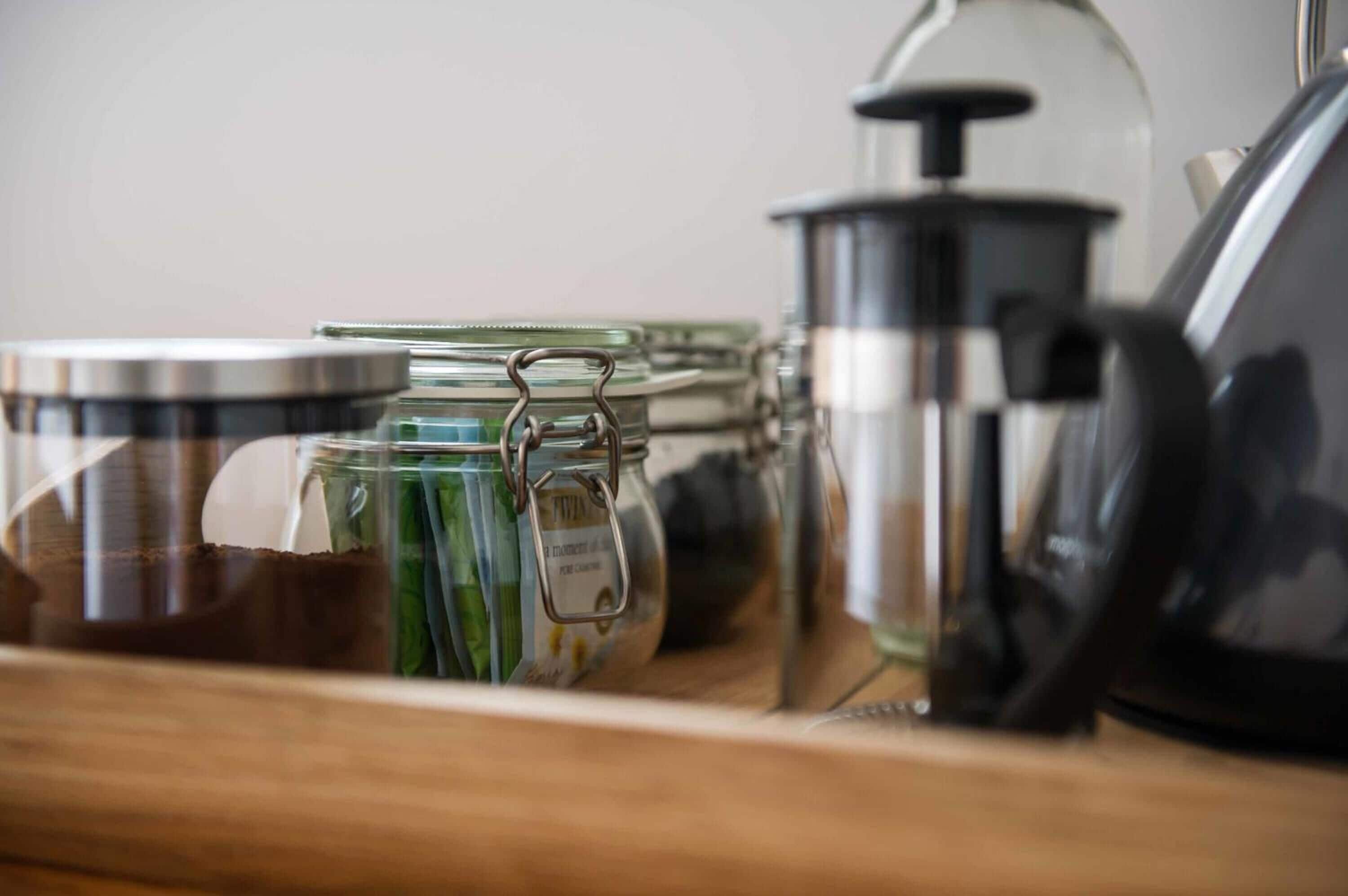 Een keukenkastje met glazen potten, een koffiepot en een waterkoker.
