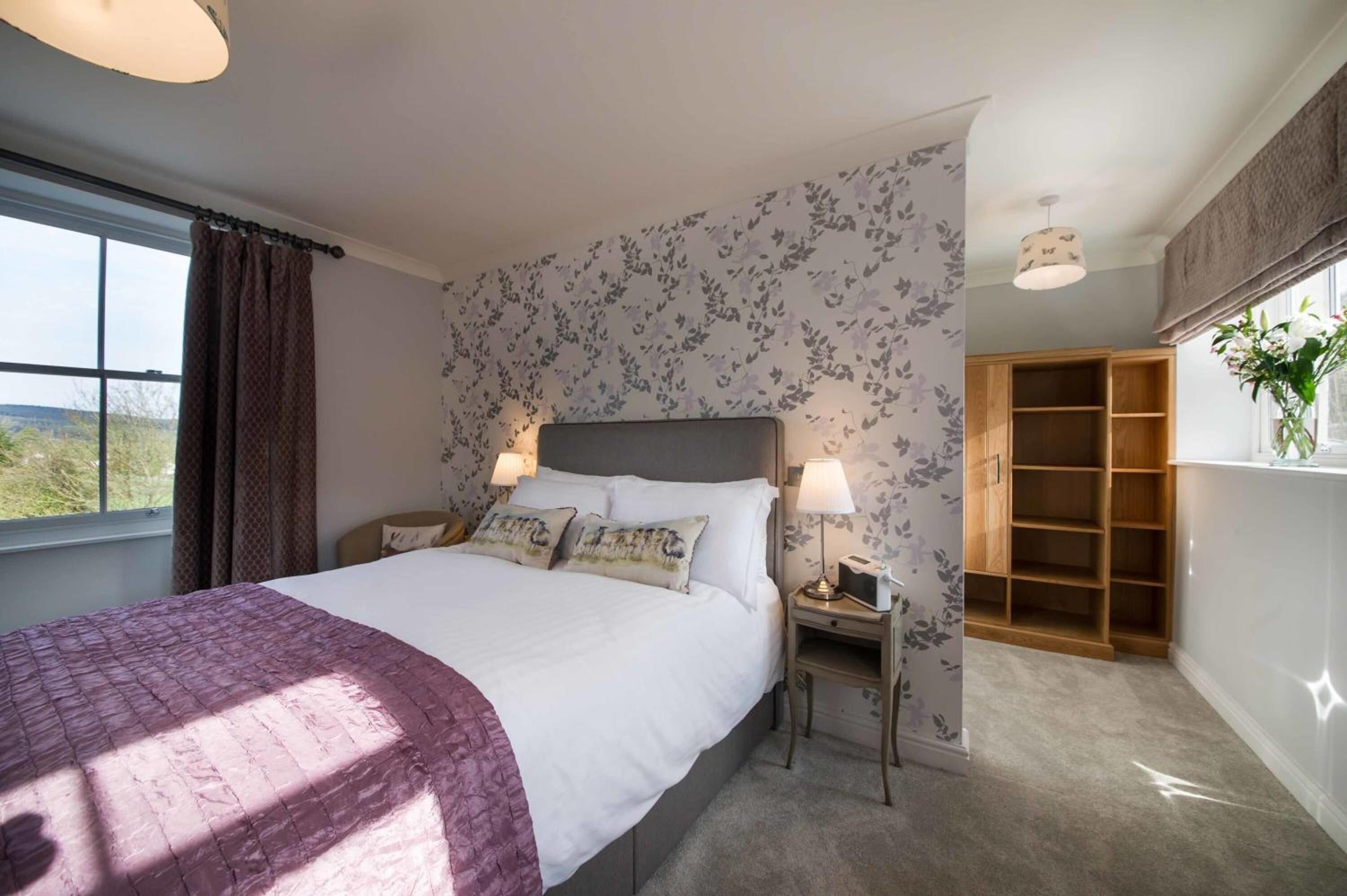 Un dormitorio con una cama grande, dos mesitas de noche con lámparas, un armario de madera y una ventana con cortinas.
