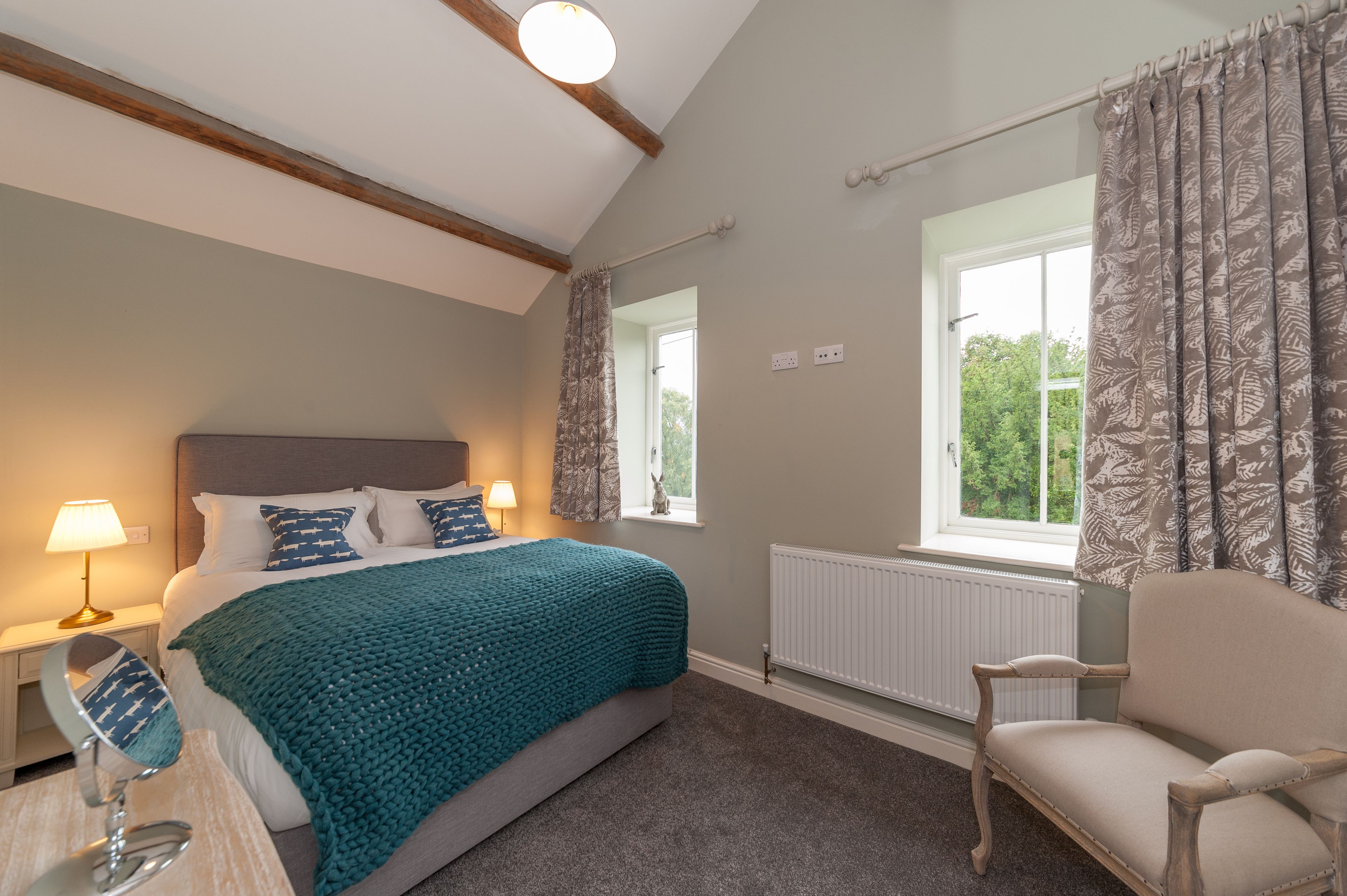 A bedroom with a bed, bedside table, lamp, chair, window, and curtains.