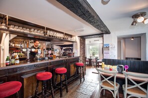 A bar area with stools, a bartender, and a variety of bottles and glasses on the shelves. - Hare & Hounds (Kendal)