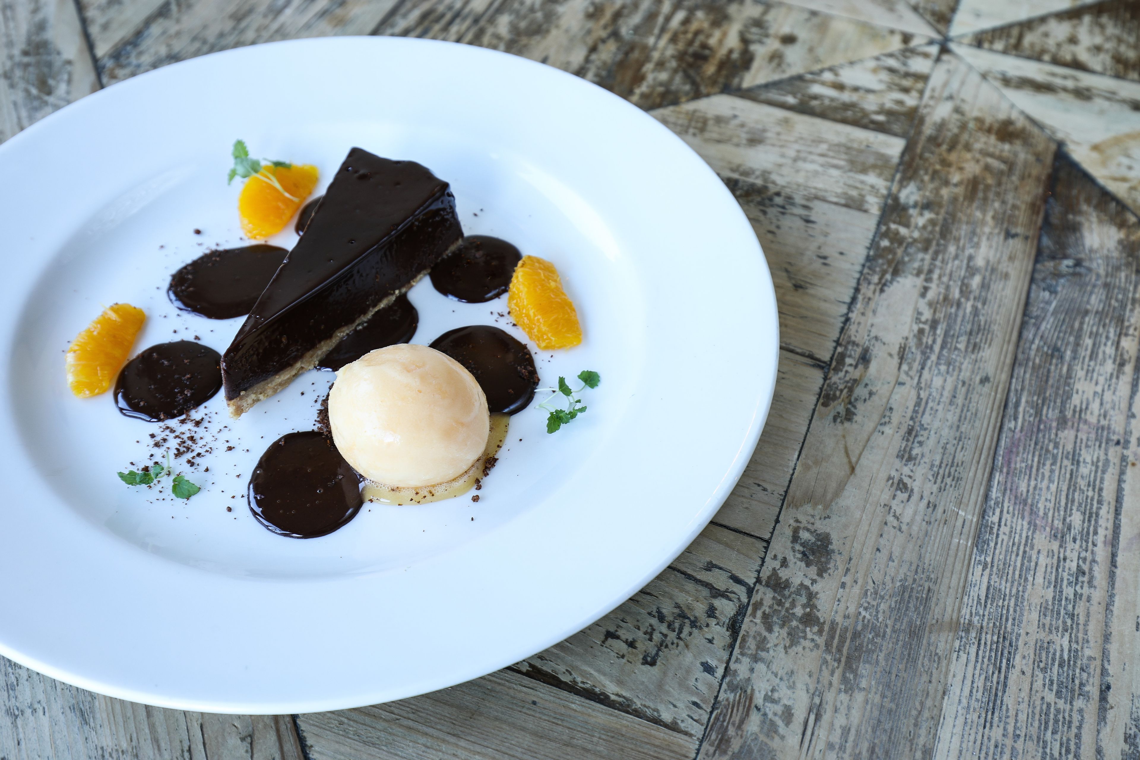 A dessert plate with chocolate pieces, orange slices, and a scoop of ice cream on a white plate.