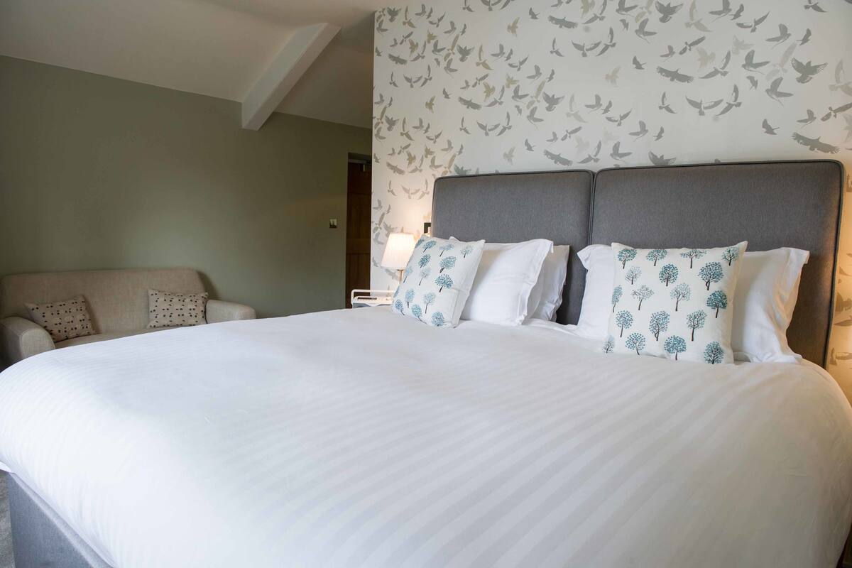 Una habitación de hotel con una cama grande, dos almohadas, una mesita de noche y una silla.